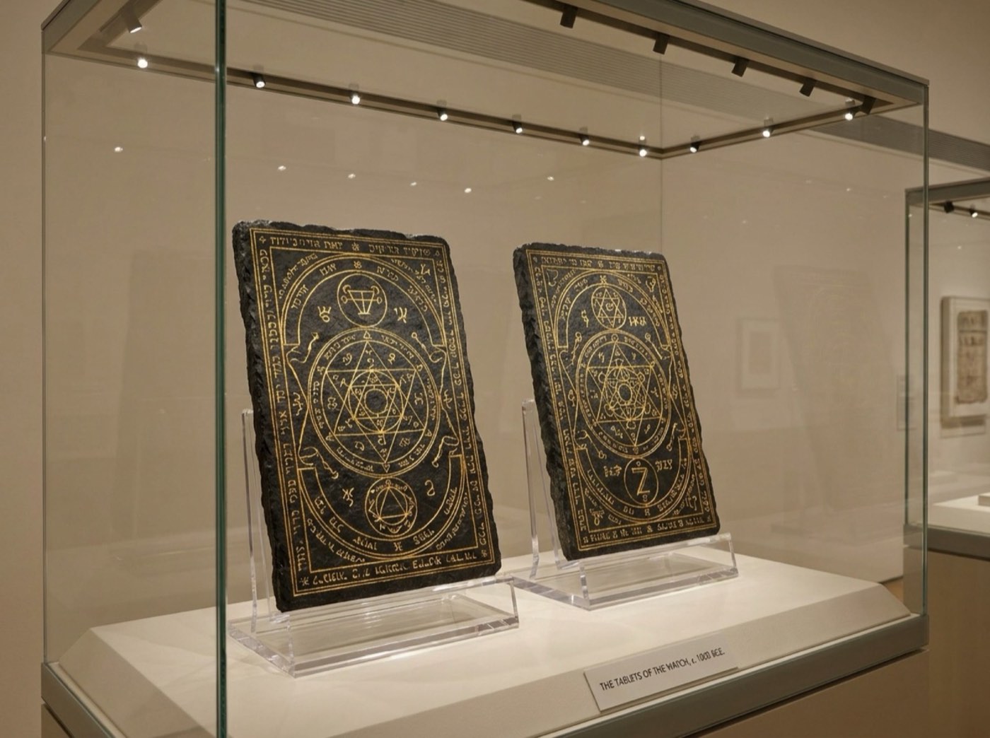 Two rectangular black stone tablets, engraved in gold with concentric Solomonic figures, upright on stands in a glass case.